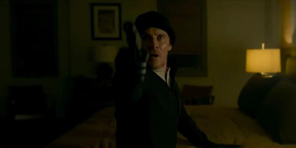 Michael Fassbender's assassin wearing all-black clothes and pointing a gun in a low-lit room in The Killer