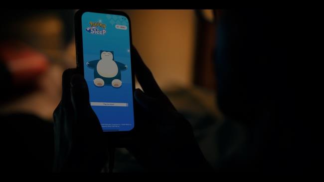 Someone holding a phone with Pokemon Sleep on the screen in a dark room