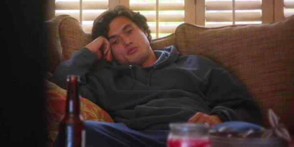 Charles Melton as Joe looking tired and listless while lying on the couch in May December